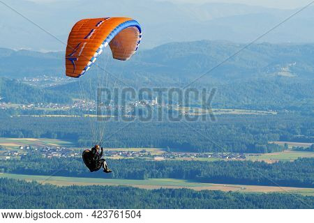 Paraglider With Orange Parachute Flying Over Countryside Before Sunset. Adrenaline, Extreme Sports A