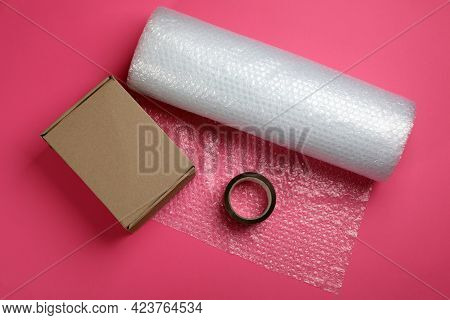 Bubble Wrap Roll, Cardboard Box And Tape On Pink Background, Flat Lay