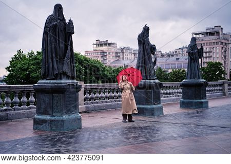 An Adult Woman With A Red Umbrella Stands Near The Sculptures At The Cathedral Of Christ The Saviour