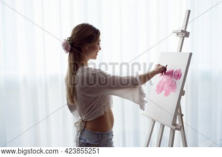 Portrait Of A Young Pragnant Woman Painting With Oil Paints On White Canvas, Side View Portrait