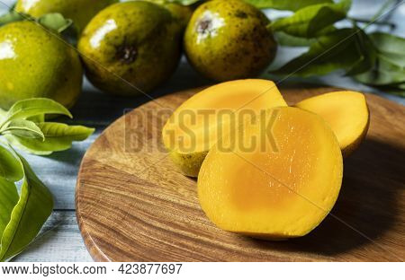 Selective Focus On Ripe Mango Slices On Wooden Chopping Board Along With Mangoes And Leaves On Woode
