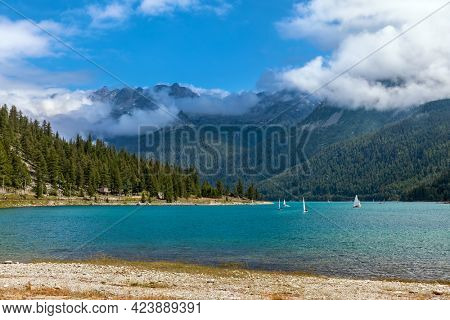 View of beautiful water on Lago di Ceresole and green trees on the mountain's slopes under blew sky with white clouds in Piedmont, Northern Italy.