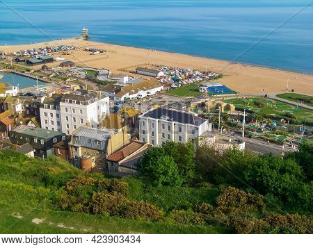 A View Of A Sunny Beach With A Town Line, A Few Beachgoers And A Calm Emerald Sea