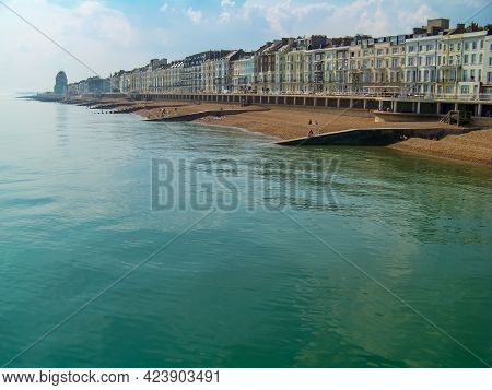 A View Of A Sunny Beach With A Town Line, A Few Beachgoers And A Calm Emerald Sea