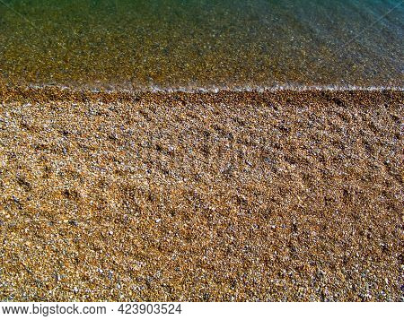 A View Of A Sunny Beach With A Town Line, A Few Beachgoers And A Calm Emerald Sea