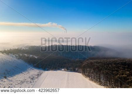 Aerial View Of Winter Landscape With Foggy Countryside And Distant Factory Pipes Emmiting Black Dirt
