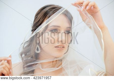 A Brunette Girl In A Wedding Dress Covers Her Face With A Veil. Bride In A White Dress. Makeup.