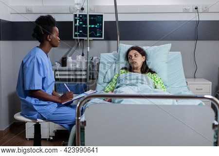 Afro American Asisstant Monitoring Sick Woman Discussing Sickness Symptom Writing Medical Expertise 
