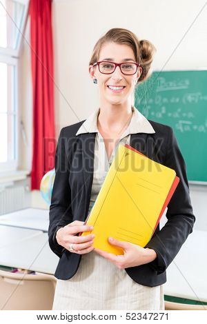Teacher or docent in school holding folder in her hands in front of a blackboard in school class