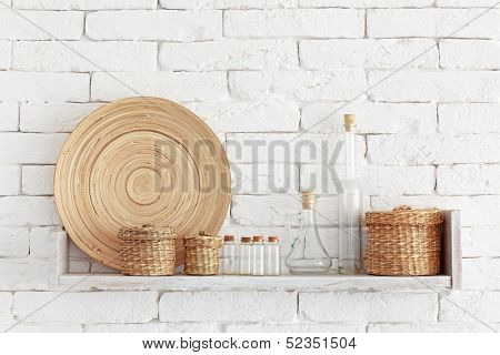 Decorative shelf on white brick wall with vintage bottles and wicker jars on it
