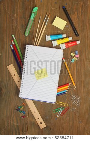 School material, pencil, rule, brushes, paper clips on a wooden table with a note book with a postite with 