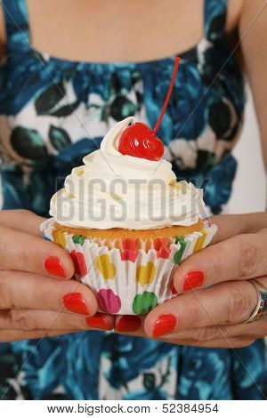 Woman with red nails holding a vanilla cupcake with cherry on top