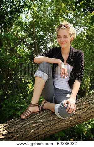 Beautiful blonde teenager sit on a tree