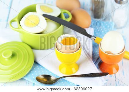Boiled eggs in pan and eggcup on color wooden background