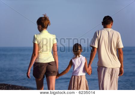 Familie mit Mädchen Spaziergänge entlang Meerstrand. Rückansicht.