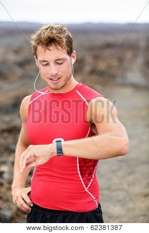 Running man looking at heart rate monitor GPS watch. Runner listening to music in earphones wearing red compression t-shirt top.