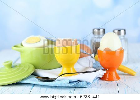 Boiled eggs in pan and eggcup on color wooden table, on light background