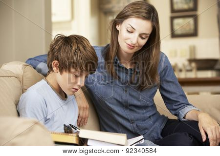 Mother Helping Son With Homework Sitting On Sofa At Home