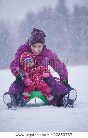 happy family on winter vacation, mom and cute little girl have fun and slide while snow falkes falling