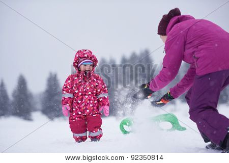 happy family on winter vacation, mom and cute little girl have fun and slide while snow falkes falling