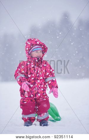 happy family on winter vacation, mom and cute little girl have fun and slide while snow falkes falling