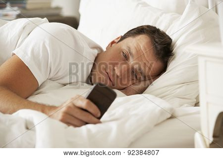 Man In Bed At Home Texting On Mobile Phone