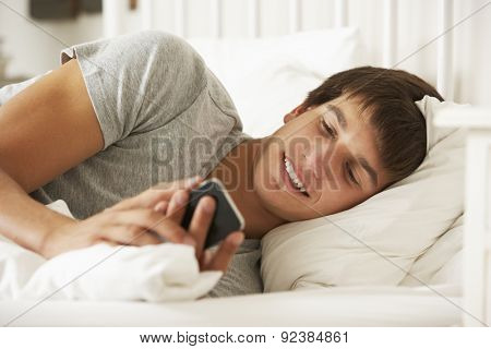 Teenage Boy In Bed At Home Texting On Mobile Phone