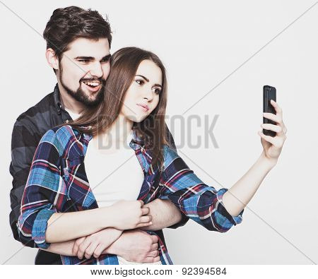 tehnology, internet, emotional  and people concept: Capturing happy moments together. Happy young loving couple making selfie and smiling while standing against white background.
