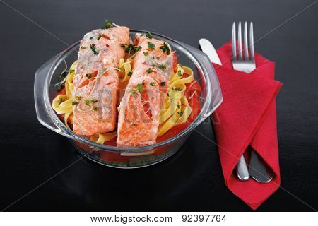 fresh fried natural pink salmon on italian traditional tagliatelle backed with tomato and vegetables served over black wooden table