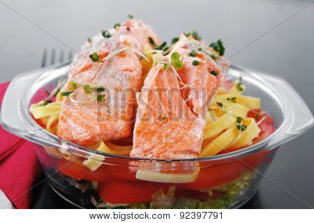 fresh fried natural pink salmon on italian traditional tagliatelle backed with tomato and vegetables served over black wooden table