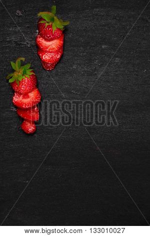 Sliced strawberries with leaves on black backfround. Top view frame. Copy space. Summer fruit food frame.
