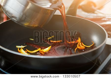 Liquid pouring on frying pan. Orange peel and red liquid. Preparing ingredients for special sauce. Wine mixed with orange skin.