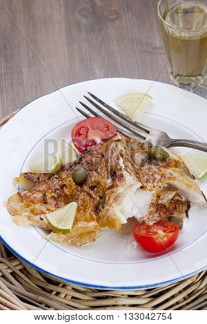 Baked fish with capers tomato and lime on a white plate
