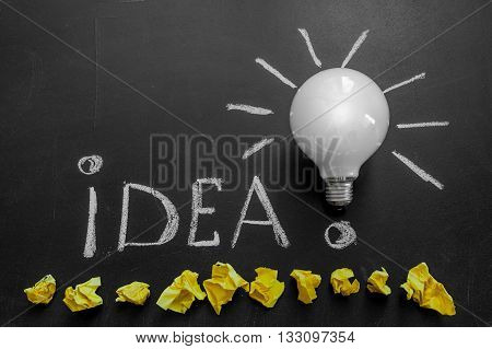 Light bulb with rays on the black chalkboard with title idea! written by white chalk and crumpled yellow papers light bulb idea business idea business concept Innovation concept