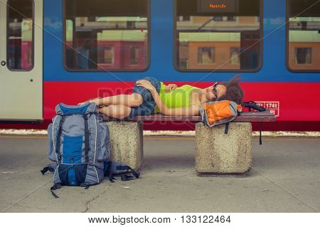 Beautiful female backpacker tourist napping on a bench and baggage at the station