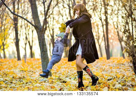 Heppy mother stends with a cheerful toddler in the park in autumn.