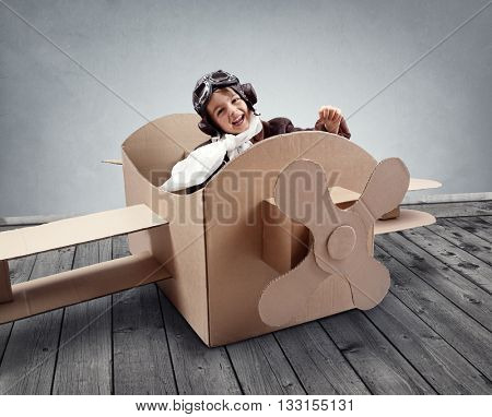 Boy wearing old-fashioned aviator hat, scarf and goggles flying a cardboard airplane in his imagination