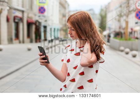 Front view of a fashion happy girl walking and using a smart phone on a city street