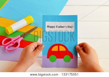 Card that said Happy father's day. Greeting card made by a kid. Child holding a greeting card for dad. Hand paper crafts. Set of colored paper, glue stick, scissors. Set for kids art implementation
