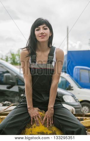 Portrait of beautiful cheerful girl in working uniform sitting in the street near the car at the service center