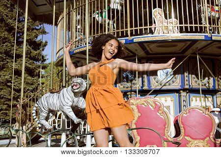 cool real modern teenage girl with candy near carousels at amusement park walking, having fun