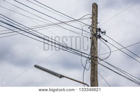 Electricity pole and street light complicated wiring With orange sunset in dark clouds.