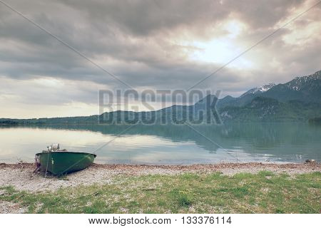 Abandoned Fishing Paddle Boat On Bank Of Alps Lake. Morning Lake Glowing By Sunlight.