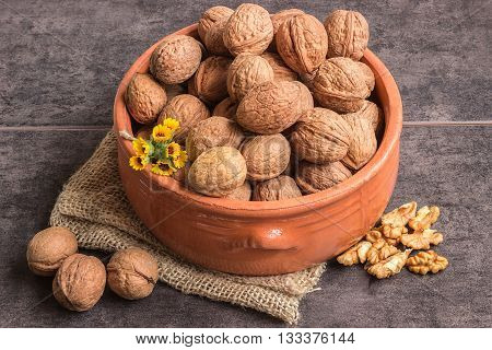 Walnuts in a ceramic bowl and a small bouquet of wild flowers on a dark background