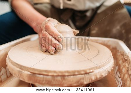 Spinning potters wheel with clay and hand. Close-up of craftsman hand on clay, shaping it into pottery. Dirty potters hand on loam of clay