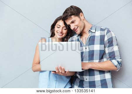 Portrait of happy young couple using laptop isolated on gray background