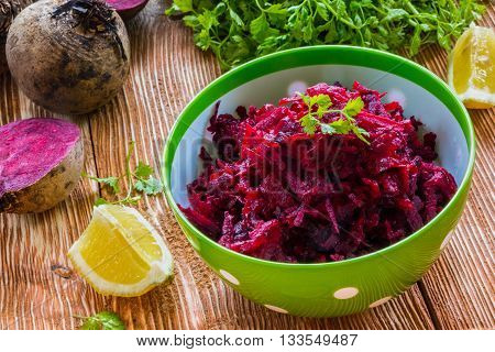 Salad: diet salad with beetroot, olive oil and lemon. Served in a bowl on wooden background. Beetroots, lemon and lettuce on kitchen table.