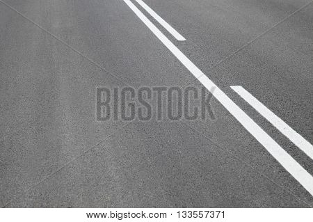 Abstract close up image of paved road with black tarred surface and white painted dividing lines to indicate driving lanes