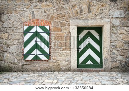 Old stone wall with wooden door and window painted in white and green.