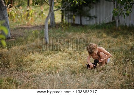 The little boy irons a tiny puppy. The child squats. Before him a tiny black puppy. The boy tenderly irons the fluffy friend.